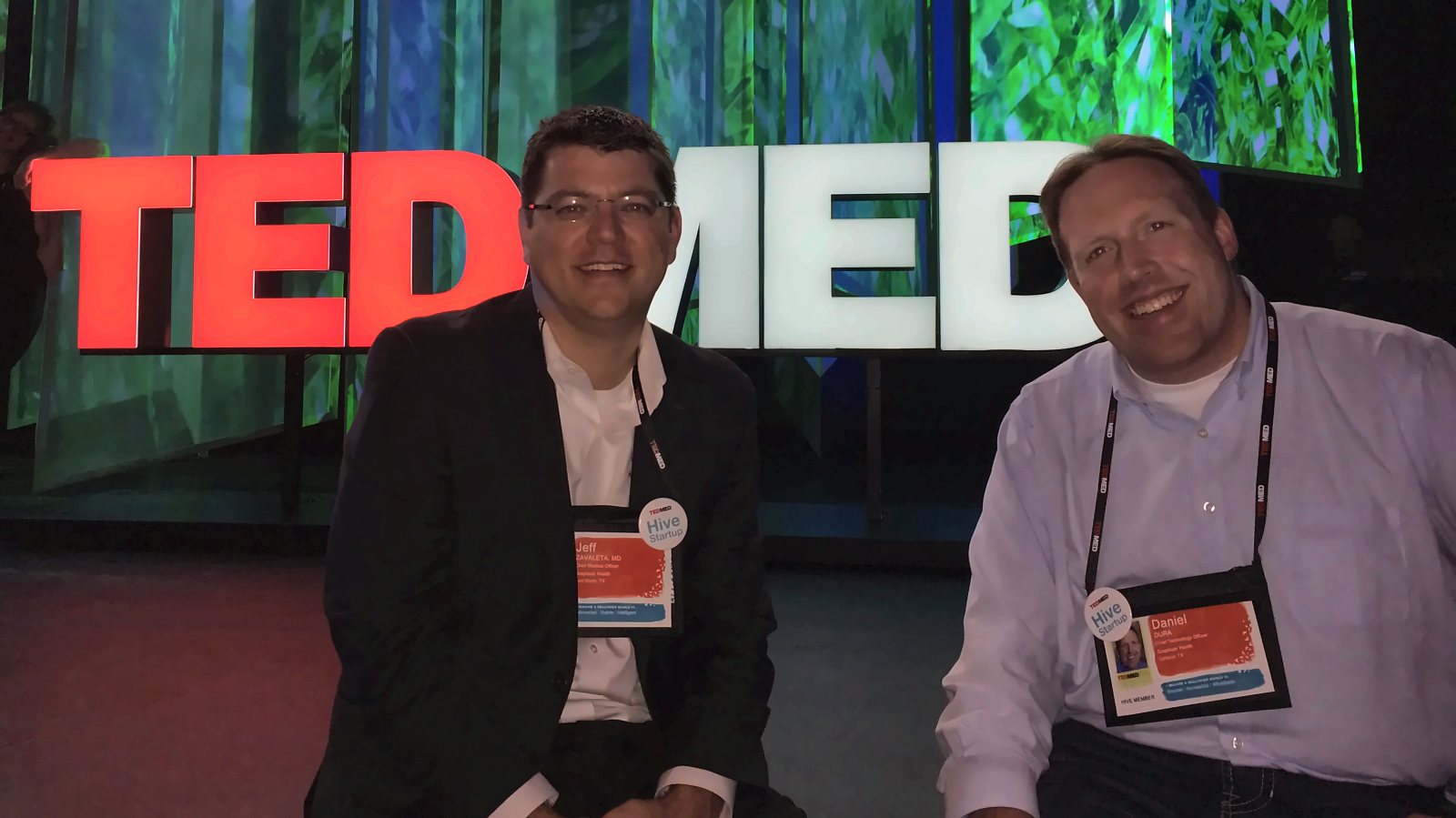 Jeff Zavaleta, MD, and Daniel Dura seated in front of the TEDMED sign, 2014