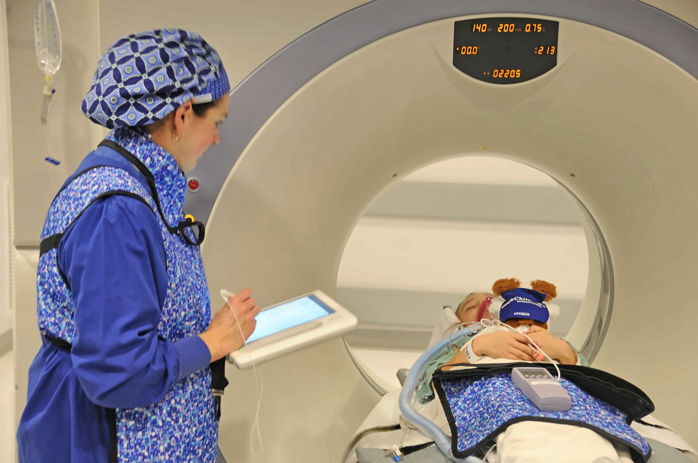 A CRNA charting on the original Windows tablet while a pediatric patient is scanned in CT